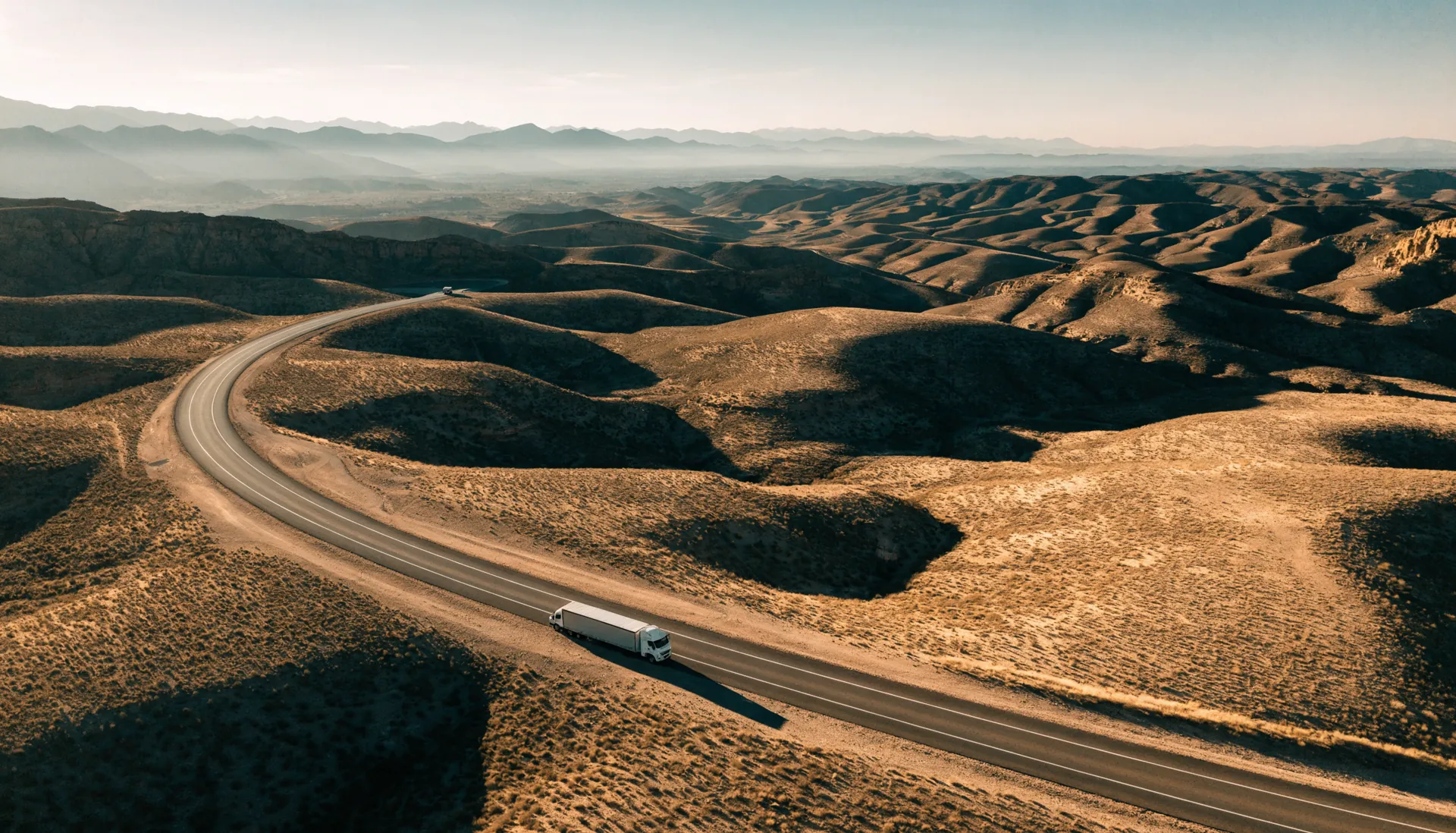 Vista aérea de una carretera federal curvándose por el altiplano árido mexicano con un tractocamión en ruta